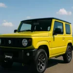 雲ひとつない青空の下、見晴らしの良い高原の道に停められたスズキジムニーJB64。ローアングルから撮影され、力強くスタイリッシュな印象を与える。